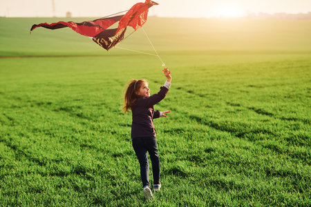 Happy little girl running with kate in hands on the beautiful fieldの写真素材
