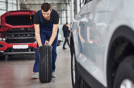 Worker in black and blue uniform is with car wheel working indoorsの写真素材