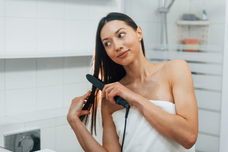 Young brunette standing on the kitchen and straightens her hairの写真素材
