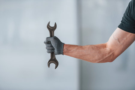 Close up view of man in grey uniform with wrench in hand indoors in modern big office at daytimeの写真素材