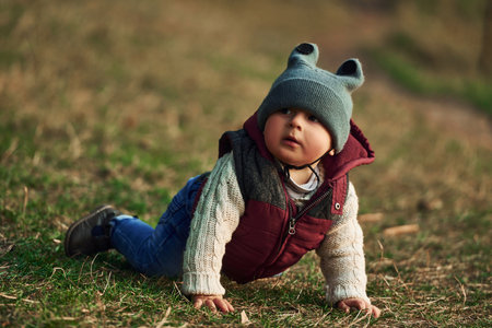 Little boy in warm clothes lying down on ground of field on grassの写真素材