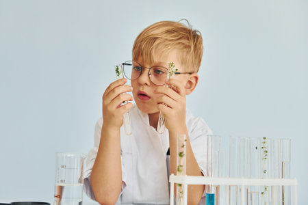 Uses test tubes. Little boy in coat playing a scientist in lab by using equipmentの写真素材