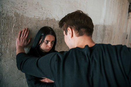 Kidnapped woman standing near wall and threatened by man with in abandoned buildingの写真素材