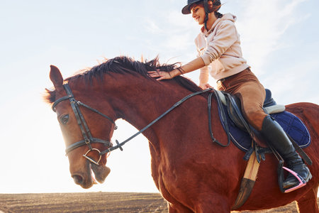 Young woman in protective hat with her horse in agriculture field at sunny daytimeの写真素材
