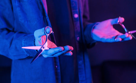 Close up view of barbers hands that holding scissors. Neon lightingの写真素材