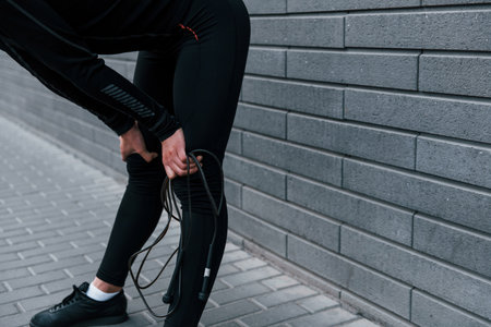 Young sportive girl in black sportswear standing with jump rope in hands outdoors near gray wallの写真素材