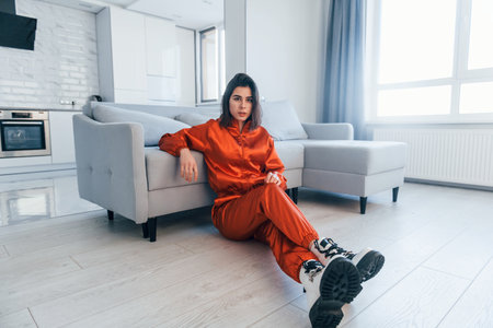 Posing for a camera in red costume. Young woman is indoors in room of modern house at daytimeの写真素材