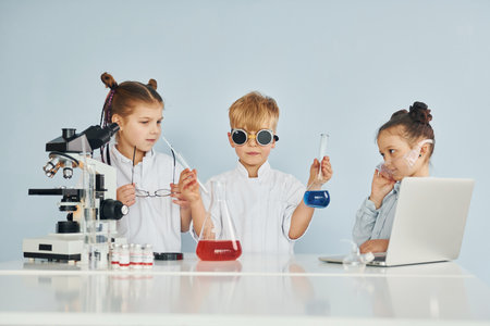 Standing by the table with test tubes. Children in white coats plays a scientists in lab by using equipmentの写真素材