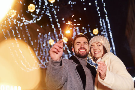 With sparklers in hands. Happy young couple celebrating New year outdoors on the streetの写真素材