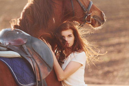 Young woman embracing her horse in agriculture field at sunny daytimeの写真素材