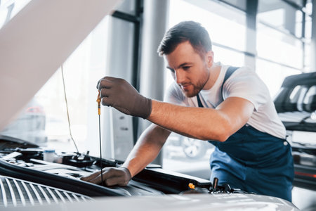 Quality service. Young man in white shirt and blue uniform repairs automobileの写真素材