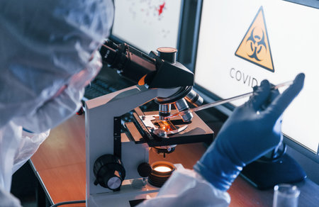 Scientist in white protective uniform works with coronavirus and blood tubes in laboratory