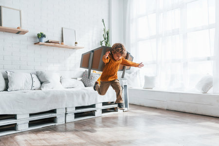 Little boy in retro pilot uniform running with toy plane indoorsの写真素材