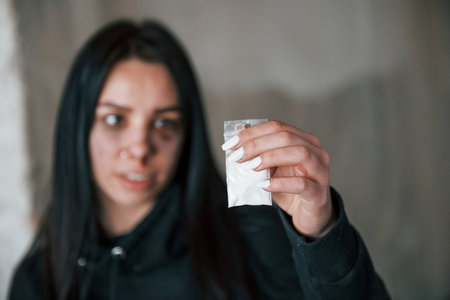 Beaten young woman holding package with white drugs in handの写真素材