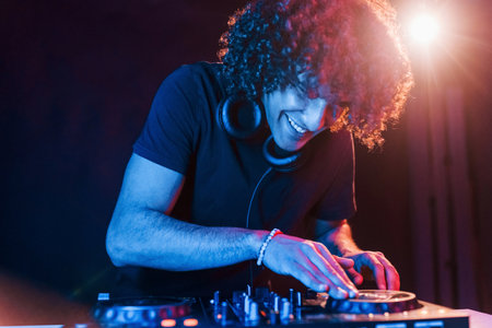 Man with curly hair using DJ equipment and standing in the dark neon lighted roomの写真素材