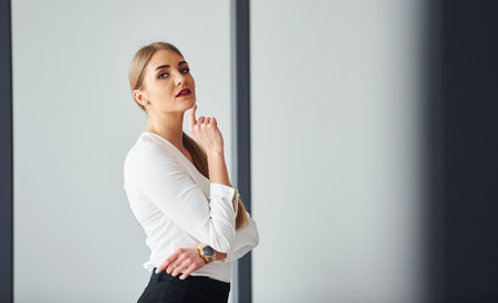 Standing against grey background. Young adult woman in formal clothes is indoors in the officeの写真素材