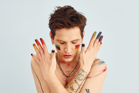 Young gay man is standing in the studio and posing for a camera. Shirtless guy with rainbow make upの写真素材