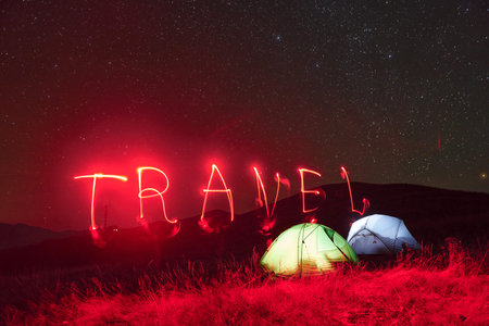 Red neon travel word. Two iluminated tents under stars at mountains at nightの写真素材