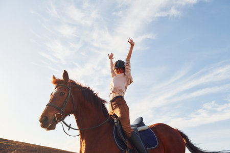 Young woman in protective hat with her horse in agriculture field at sunny daytimeの写真素材