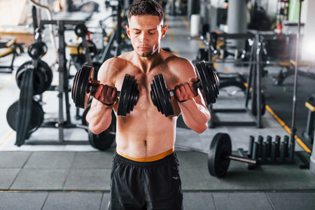 Liting dumbbells. Young sportive strong man in black wear have workout day in gymの写真素材
