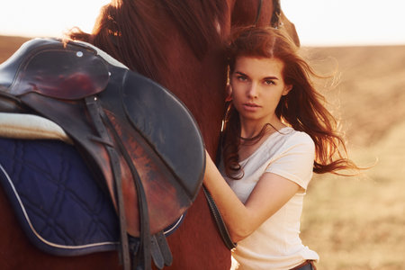 Young woman embracing her horse in agriculture field at sunny daytimeの写真素材
