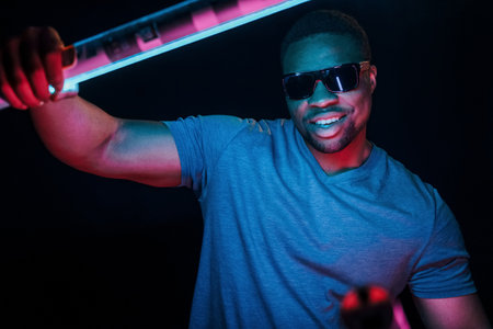 With sunglasses. Futuristic neon lighting. Young african american man in the studioの写真素材
