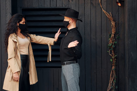 Woman with black curly hair standing against black wooden building exterior with her man in hatの写真素材