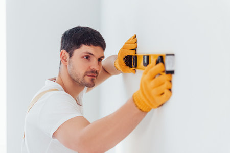 Handyman in yellow uniform checks levels of wall. House renovation conceptionの写真素材