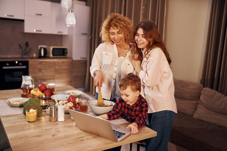 Cheerful people having happy weekend. Family of mother, daughter and son is on the kitchen at evening timeの写真素材
