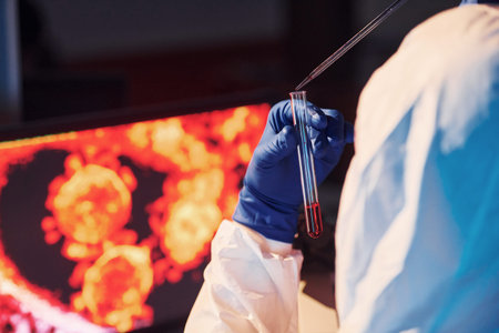 Scientist in white protective uniform works with coronavirus and blood tubes in laboratory