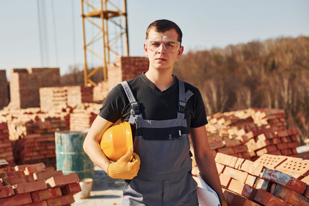 Portrait of construction worker in uniform and safety equipment that stands on rooftop of unfinished...