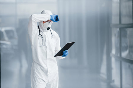 Tired doctor scientist in lab coat, defensive eyewear and mask takes breakの写真素材
