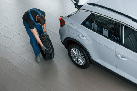 Top view of worker in black and blue uniform that is with car wheel working indoorsの写真素材