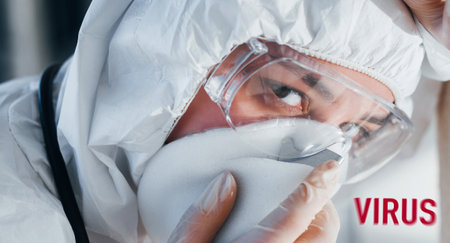 Red virus word. Nurse in protective uniform, mask and glasses standing indoorsの写真素材