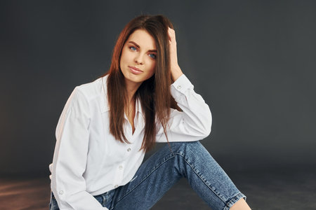 In white shirt and blue jeans. Young beautiful woman is posing for the camera in the studioの写真素材