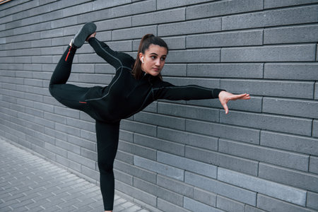 Young sportive girl in black sportswear outdoors doing yoga exercises near gray wallの写真素材