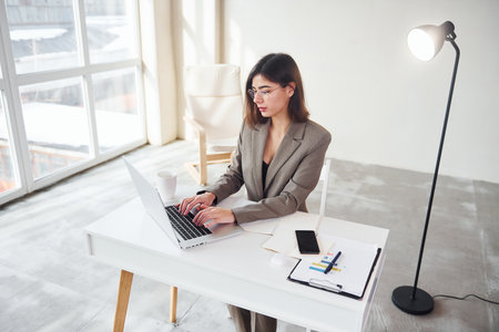 Works in the office by laptop. Young woman in formal clothes is indoors. Conception of styleの写真素材
