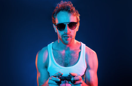 Having fun. Neon lighting. Young european man is in the dark studioの写真素材