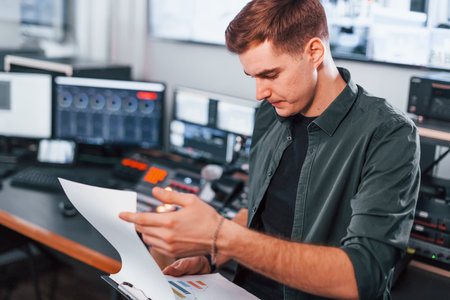 Document with scenario. Young man is indoors in the radio studio is busy by broadcastの写真素材