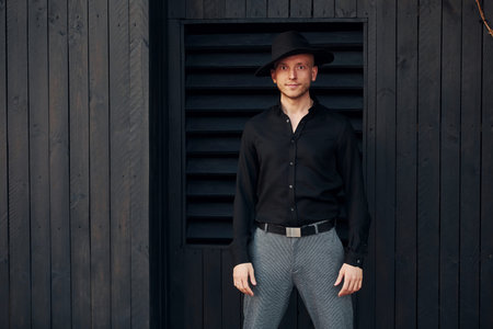 Man in black hat standing against black wooden building exterior