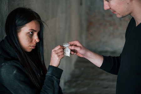 Two people standing with illegal drugs in little package indoorsの写真素材