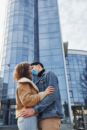 Couple in protective masks kissing each other in the city near business building at quarantine time. Conception of coronavirusの写真素材