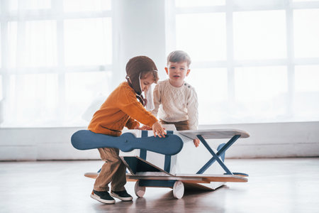 Two little boys in retro pilot uniform having fun with toy plane indoorsの写真素材