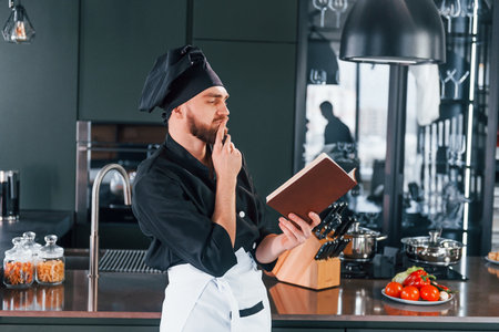 Professional young chef cook in uniform standing with notepad on the kitchenの写真素材