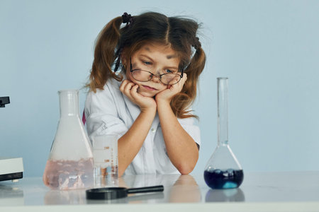 Unsuccessful experiment. Little girl in coat playing a scientist in lab by using equipment