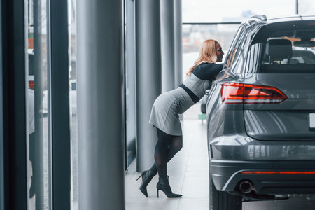 Beautiful blonde in elegant clothes standing near new modern carの写真素材
