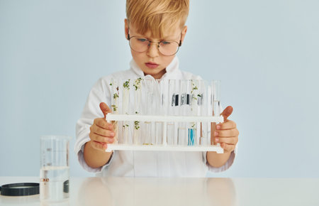 Uses test tubes. Little boy in coat playing a scientist in lab by using equipmentの写真素材