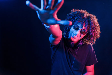 Young beautiful man with curly hair is indoors in the studio with neon lighting