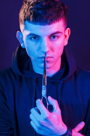 Holds scissors. Young barber with work equipment standing in the studio with neon lightingの写真素材