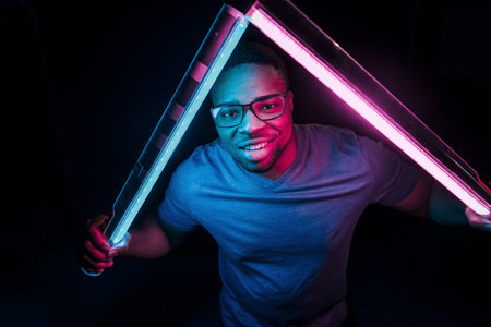 Holds lighting equipment. Futuristic neon lighting. Young african american man in the studioの写真素材